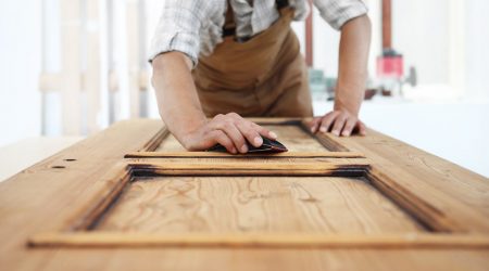 Tischler schleift mit der Hand eine Holztür ab