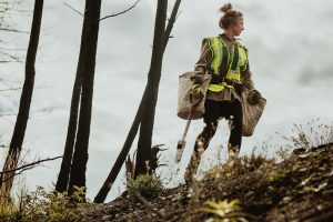 Forstwirtin in Arbeitskleidung in einem Wald und pflanzt Bäume ein.