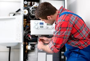 Heizungsinstallateur in blauer Arbeitshose bei der Wartung einer Heizungsanlage