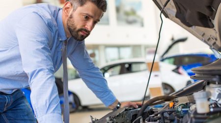 Mann mit Hemd und Krawatte beugt sich über den Motor eines Autos