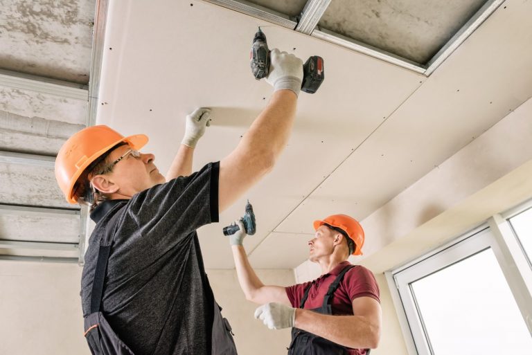 Trockenbauer mit orangenen Bauhelmen beim Abhängen einer Decke mit Akkuschraubern