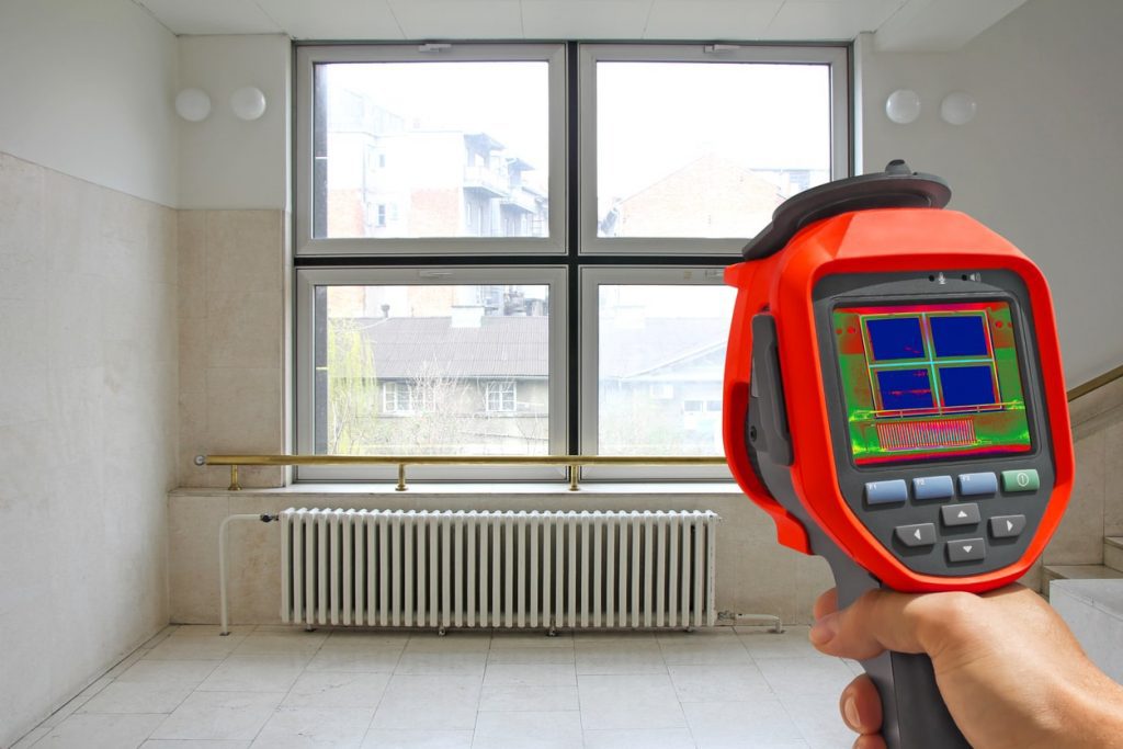 Eine Wärmebildkamera wird in einem Wohnhaus vor Fenster gehalten um Wärmeverluste zu entdecken