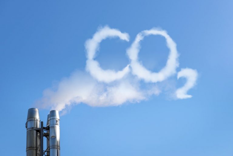 Rauch steigt in Form eines CO2 Schriftzugs aus einem Industrie Schornstein