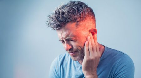 Mann mit grauen Haaren hält sich schmerzverzerrt die Hand aufs Ohr