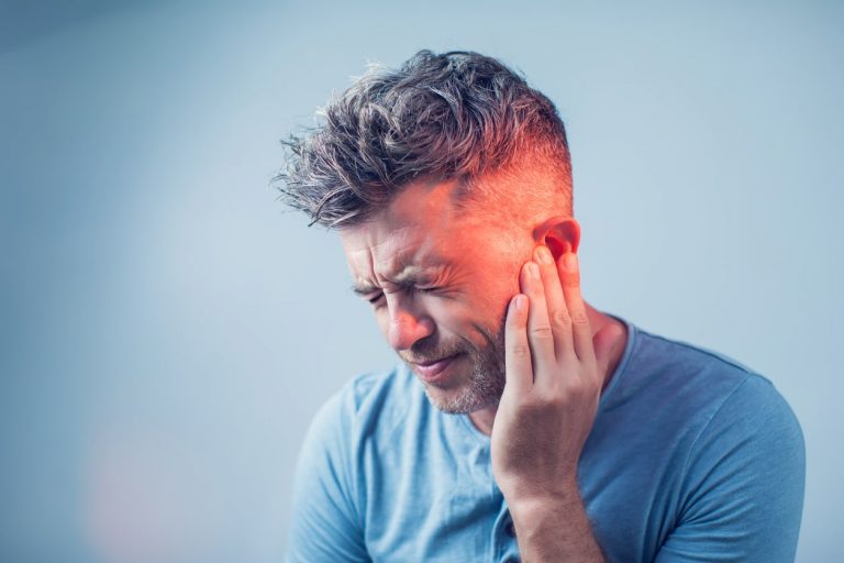 Mann mit grauen Haaren hält sich schmerzverzerrt die Hand aufs Ohr