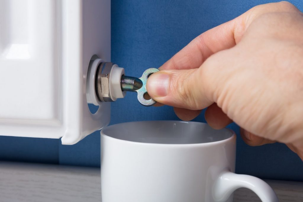 Heizung wird entlüftet mit Schlüssel und Tasse unter dem Heizkörper um Wasser aufzufangen