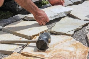 Gummihammer eines Landschaftsgärtners auf Natursteinplatten, der einen Gartenweg pflastert