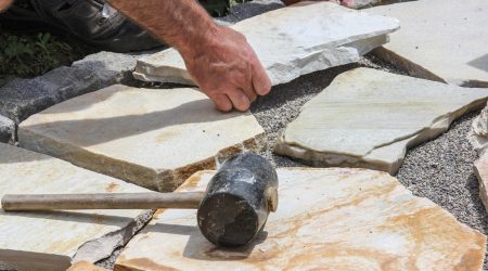 Gummihammer eines Landschaftsgärtners auf Natursteinplatten, der einen Gartenweg pflastert