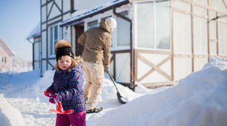 Kind im Winter räumt Schnee mit einer roten Schneeschaufel