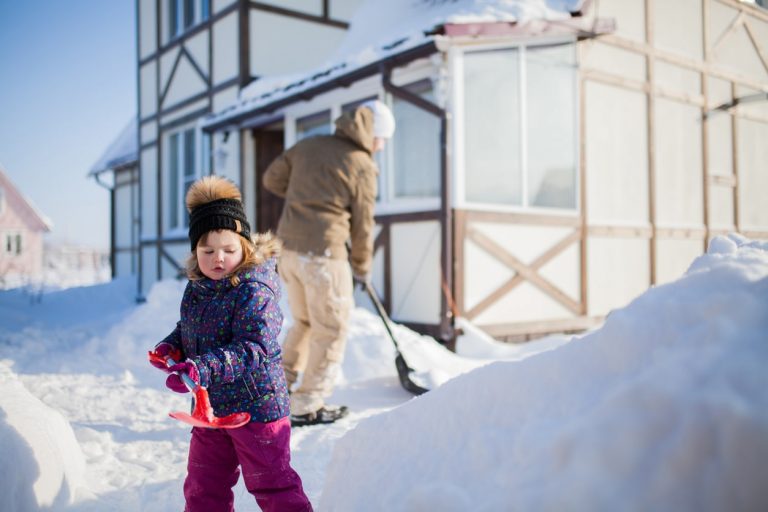 Kind im Winter räumt Schnee mit einer roten Schneeschaufel