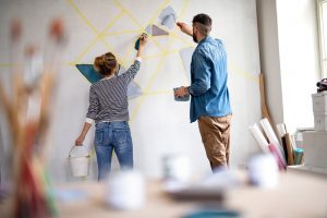 Eine Frau und eine Mann streichen gemeinsam eine vorbereitete Wand mit besonderer Technik in einer Wohnung
