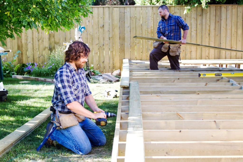 Zwei Handwerker verlegen eine Holzterrasse im Garten