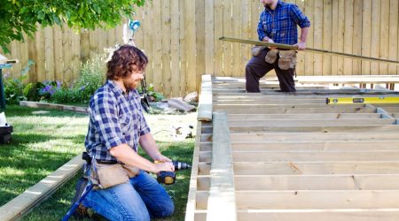 Zwei Handwerker verlegen eine Holzterrasse im Garten
