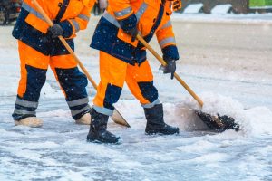 Zwei Mitarbeiter eines Winterdienst räumen mit Schneeschaufeln den Gehweg
