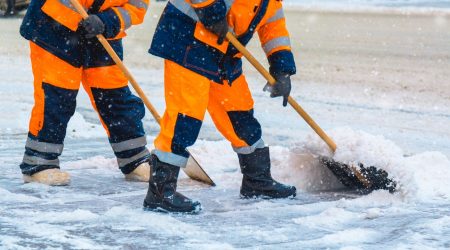 Zwei Mitarbeiter eines Winterdienst räumen mit Schneeschaufeln den Gehweg