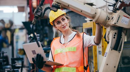 Frau mit Helm und Uniform mit Laptop-Kontrolle an Maschine