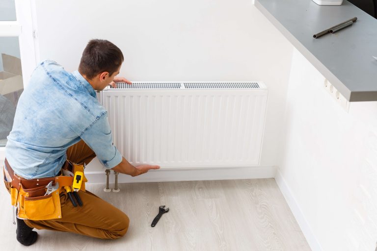 Mann montiert Heizkörper an einer Wand