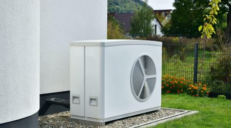 Luftwärmepumpe steht im Garten vor einem Haus