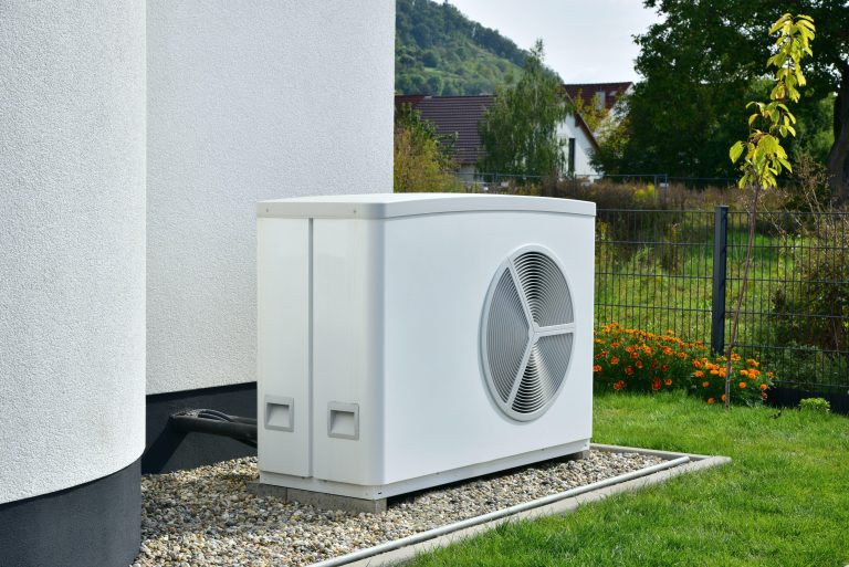 Luftwärmepumpe steht im Garten vor einem Haus