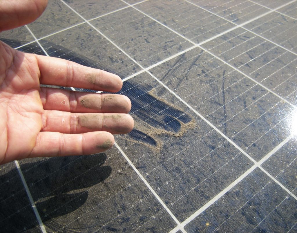 Hand zeigt Staub auf Photovoltaik