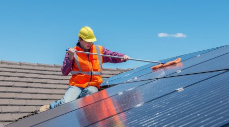 Mann reinigt Photovoltaik Anlage auf einem Hausdach