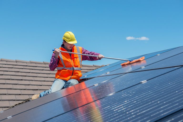 Mann reinigt Photovoltaik Anlage auf einem Hausdach