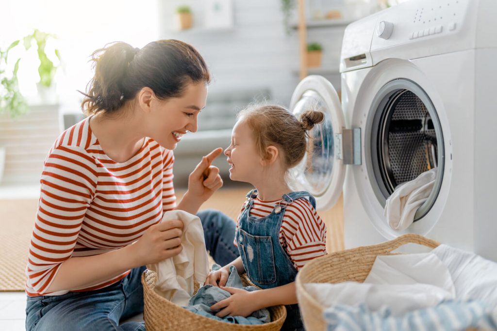 Mutter sitzt mit Tochter vor Waschmaschine