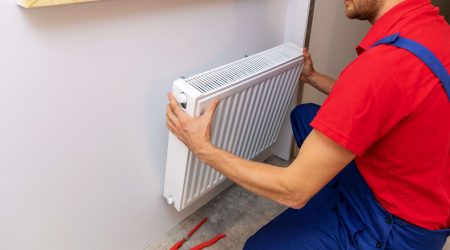 Heizungsbauer montiert Heizkörper an einer Wand