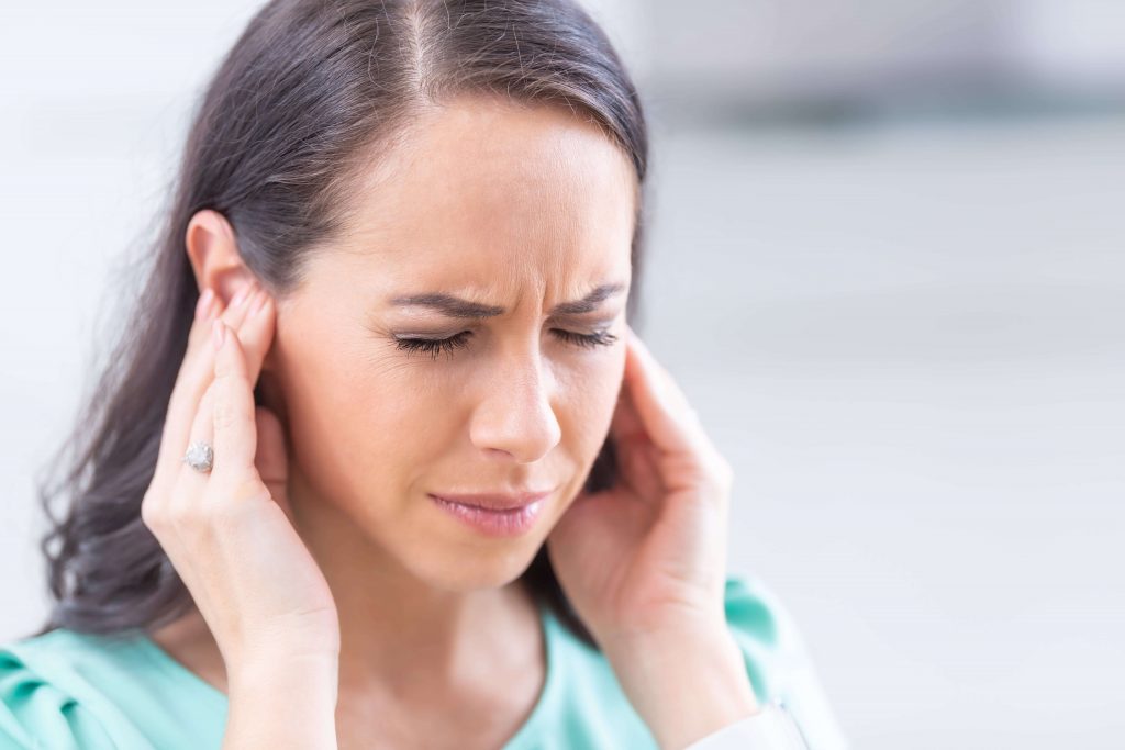 Frau hält sich die aufgrund von Tinnitus die Ohren zu
