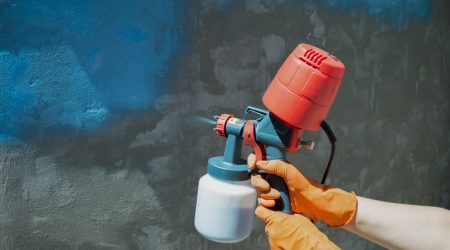 Maler sprüht Dispersionsfarbe an eine Wand