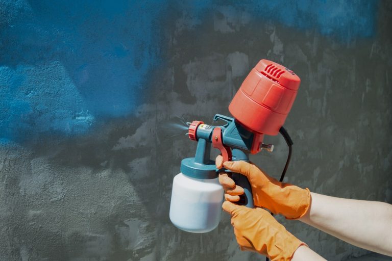 Maler sprüht Dispersionsfarbe an eine Wand