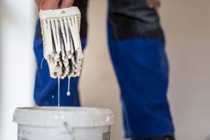 Pinsel von einem Maler in Nahaufnahme der in einen Eimer mit Haftgrundierung gehalten wird