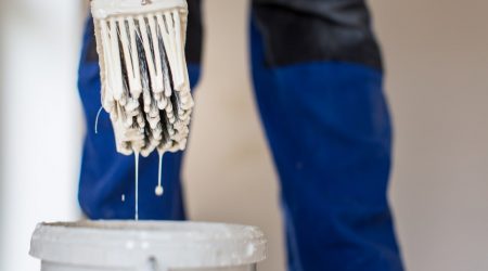 Pinsel von einem Maler in Nahaufnahme der in einen Eimer mit Haftgrundierung gehalten wird