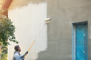 Maler grundiert eine Putzfassade mit Tiefengrund für den anschließenden Fassadenanstrich.