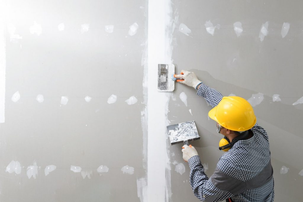 Handwerker mit gelbem Bauhelm verspachtelt eine Trockenbauwand