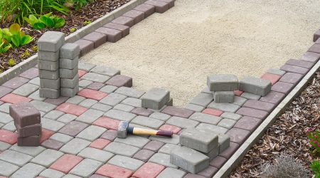 Gartenweg der gepflastert wird mit Pflastersteinen in grau und rot