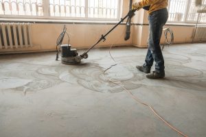 Bodenleger schleift Estrich mit einer Schleifmaschine