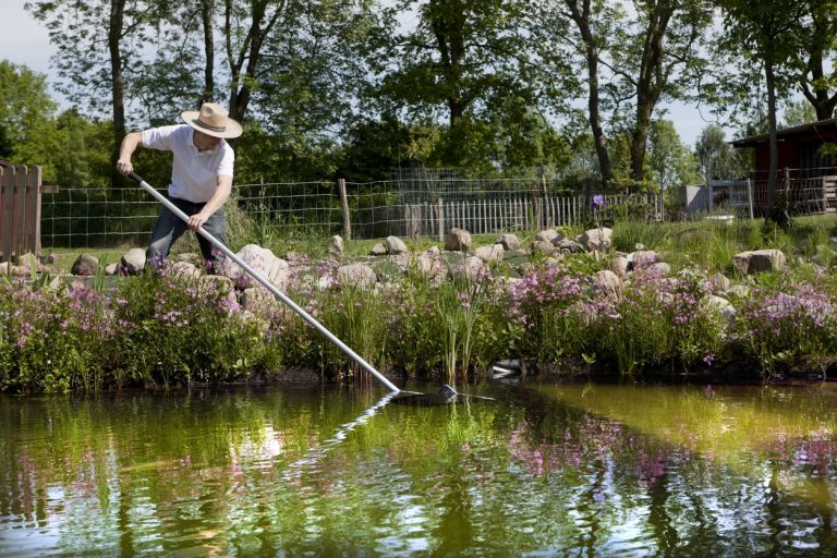 Gärtner mit Strohhut reinigt einen Gartenteich mit einem Kescher einen Gartenteich im Sommer