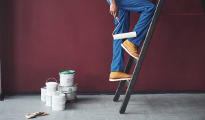 Maler mit blauer Uniform und Farbrolle steht auf Leiter