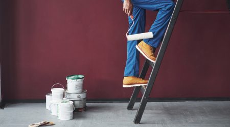 Maler mit blauer Uniform und Farbrolle steht auf Leiter