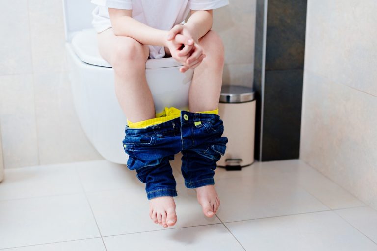 Kind sitzt auf einer Toilette mit Füßen in der Luft
