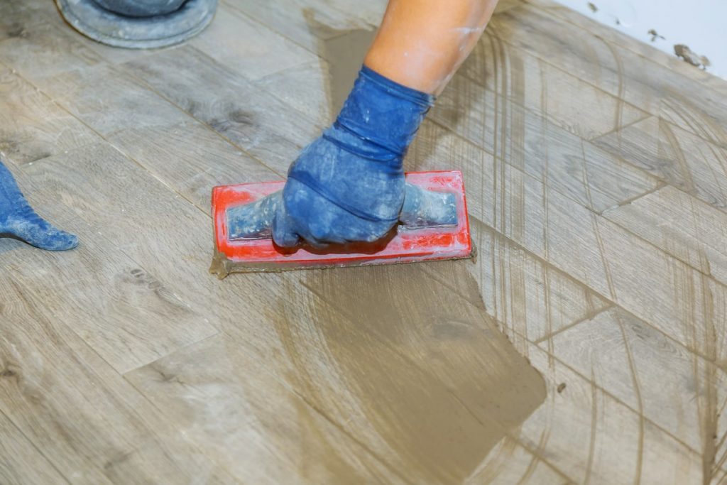 Fliesenleger mit blauen Gummihandschuhen bringt Fugenmasse auf den Boden auf