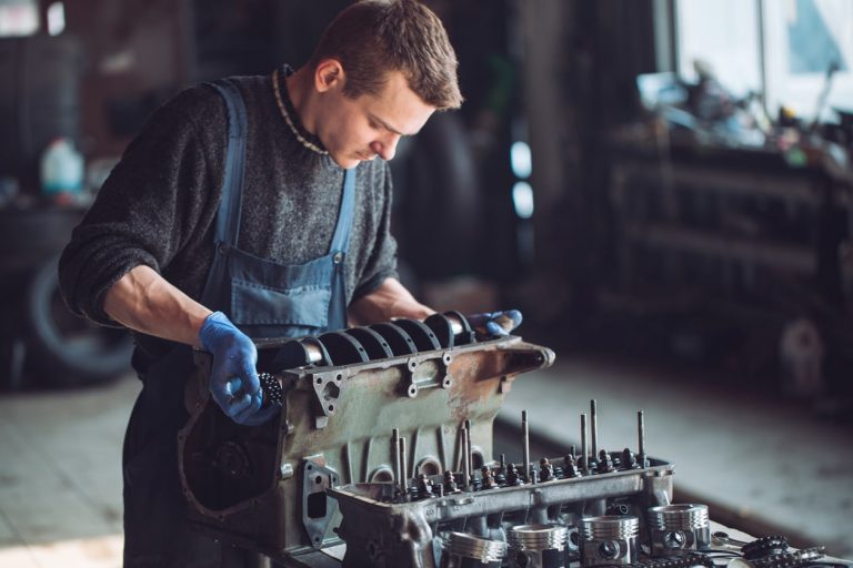 Automechaniker mit blauen Handschuhen hebt Teile eines Automotors an