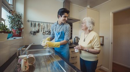 Professionelle, junge Haushaltshilfe mit älter, lachender Frau in der Küche