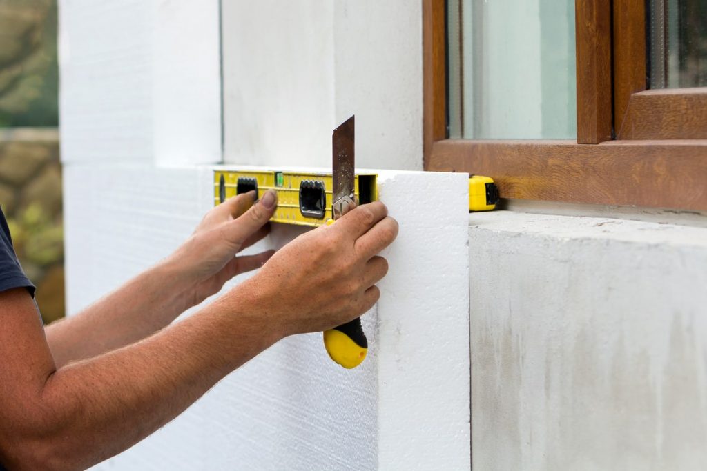 Maler bringt eine Wärmedämmung von außen an der Fassade an und schneidet diese um die Fenster aus