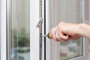 Handwerker montiert einen Fensterbeschlag an einem weißen Kunststofffenster