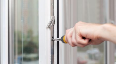 Handwerker montiert einen Fensterbeschlag an einem weißen Kunststofffenster
