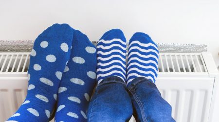 Zwei Paar Füße in blauen Socken mit Punkten und Streifen ruhen auf einem weißen Heizkörper.