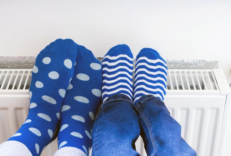 Zwei Paar Füße in blauen Socken mit Punkten und Streifen ruhen auf einem weißen Heizkörper.