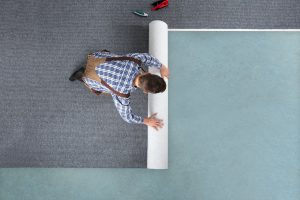 Bodenleger verlegt einen grauen Teppichboden